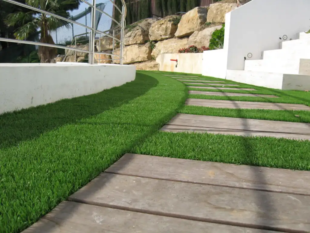 A curved pathway made of wooden planks is laid over a lush green artificial grass lawn