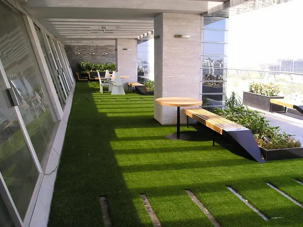 A rooftop terrace with artificial grass, featuring wooden benches, a round table, and potted plants