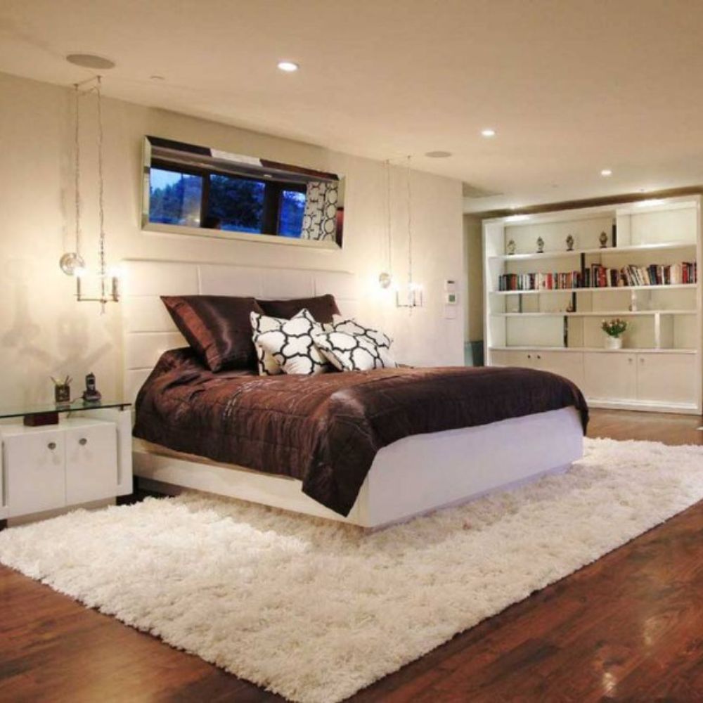 A large, luxurious bedroom with a white fluffy rug, a king-size bed, and a fireplace